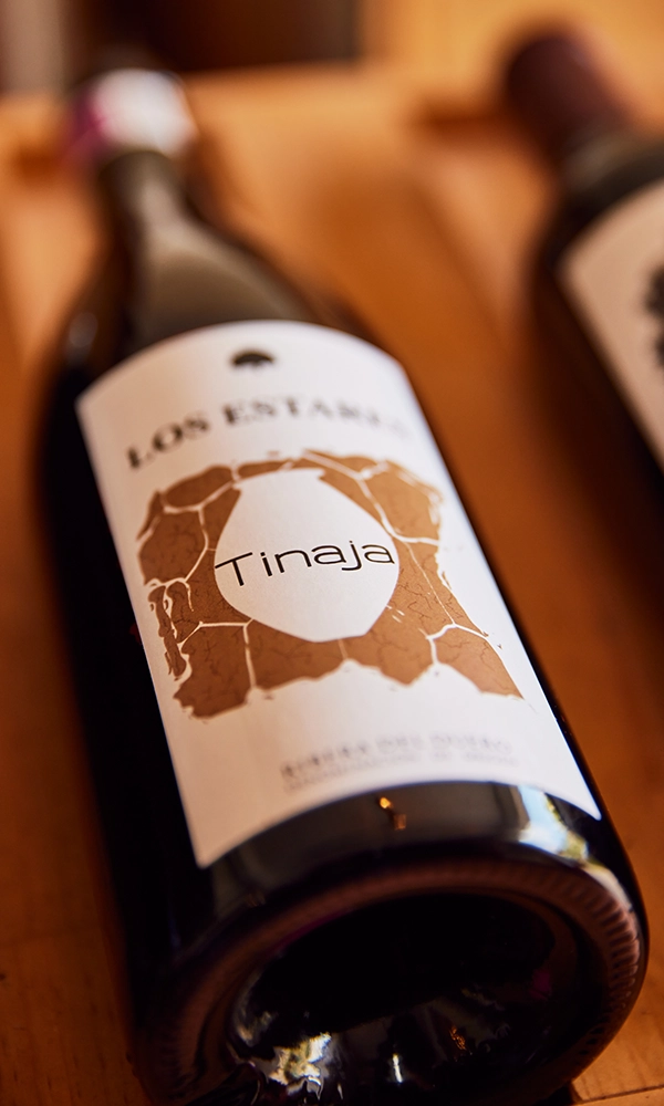 Botella de Tinaja de la Bodega de Pago de los Estares tumbada sobre una superficie de madera Botella de Tinaja de la Bodega de Pago de los Estares tumbada sobre una superficie de madera